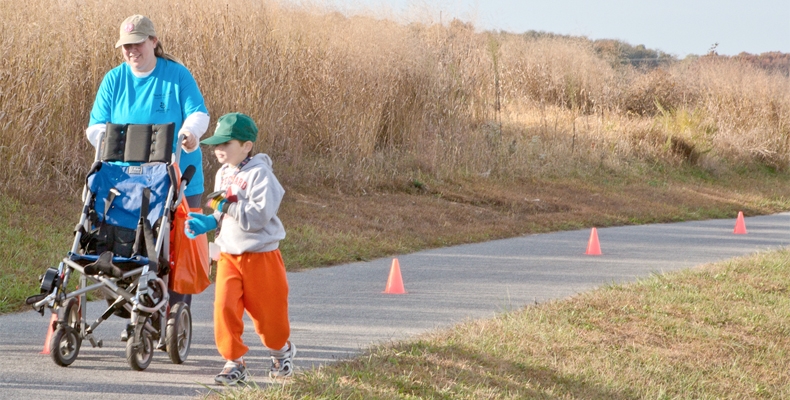 Child takes a moment to get out of his wheelchair and run alongside it while his mother pushes it.
