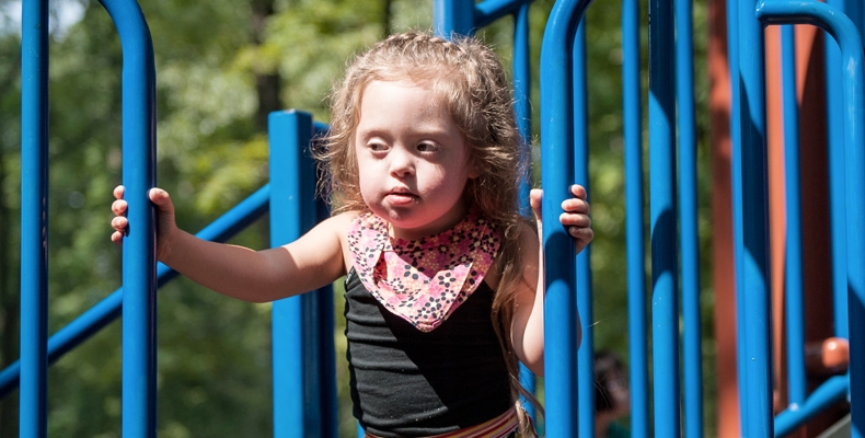 A young girl looks out across the playground from the blue jungle gym.